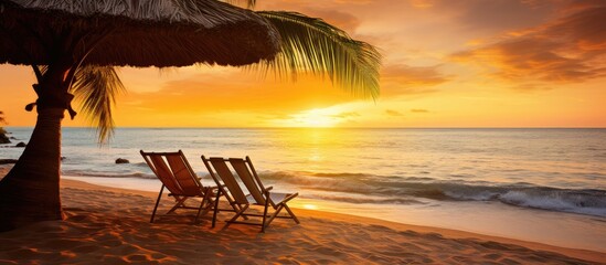 Luxurious tropical beach sunset scene with chairs, umbrella, palm leaves, and calm sea shore. Ideal vacation destination copy space image.