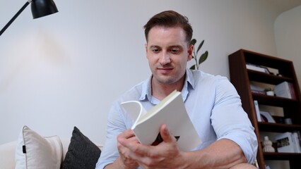 Middle age man sitting on sofa read fable book increase knowledge about social and imagination for...