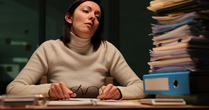 Fatigued woman looks at high stack of unprocessed documents