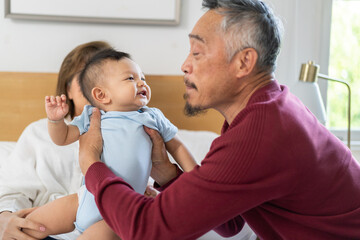 Joyful moment of multigenerational family at home, father holding up his baby smiling and playing while the grandfather looks on with a big smile enjoying the happy interaction, love within a family