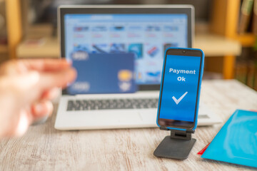 Person Showing Credit Card, Online Purchase Made With Laptop. Mobile Device Shows Secure Payment Confirmation.