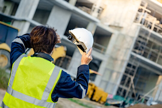 Dizziness and migraine headache from overworked exhaustion or heat stroke. Tired Asian male worker taking off safety helmet touching forehead while working at construction site in extremely hot day