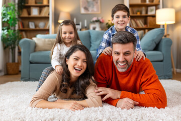 Happy parents and their small kids talking while lying on carpet at home.