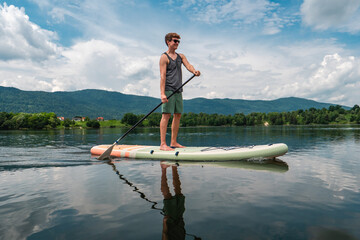 SUP Stand up paddle board concept - young men paddle boarding on lake