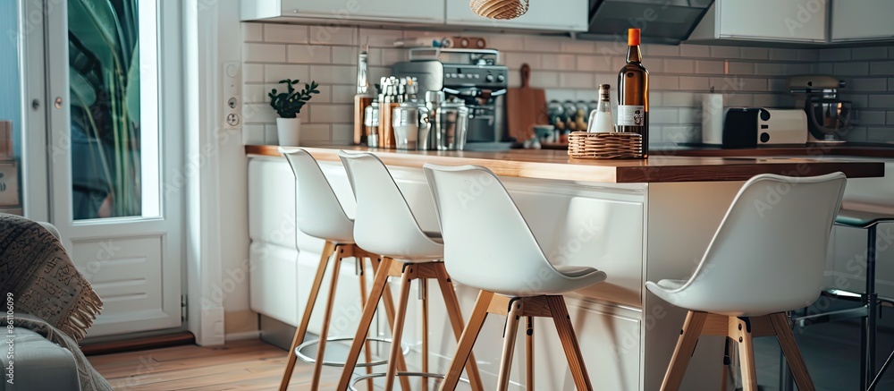 Poster bar stools at counter placed near cabinets and modern appliances in light stylish kitchen with bottl