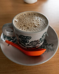 Top view of bubbles on the white coffee served in Kopitiam cup on the wooden table.