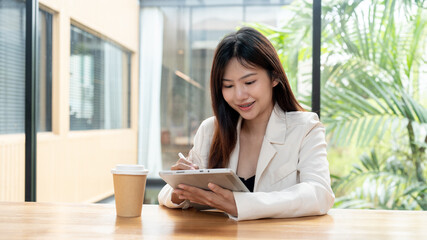 An attractive Asian businesswoman is working remotely from a coffee shop, using her digital tablet.