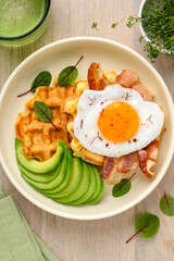 Cheese waffles, fried egg, bacon and avocado in a bowl. Balanced breakfast.  Top view