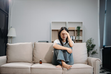 Asian woman sit Depression Dark haired  pensive glance Standing by window and anxiety Copy space with a blanket on a sofa.