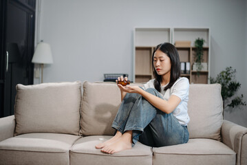 Asian woman sit Depression Dark haired  pensive glance Standing by window and anxiety Copy space with a blanket on a sofa.