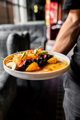 Close-up of a person holding a plate of colorful food, featuring sliced vegetables and possibly fish.