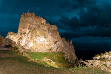 Night electric lighting of the rock and Kojori fortress. Green grass. Night sky with heavy clouds