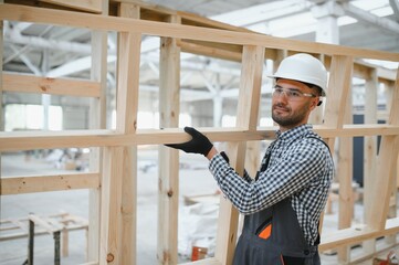 A worker or engineer in a uniform works on a construction site for the manufacture of wooden...