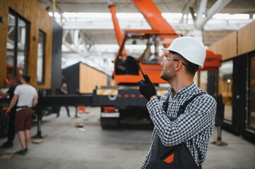 Foreman manages the loading of a prefabricated modular house to truck using walkie talkie