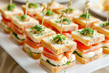Mini sandwiches with cheese, tomatoes, and fresh greens, beautifully arranged on a plate, perfect for appetizers or snacks at gatherings