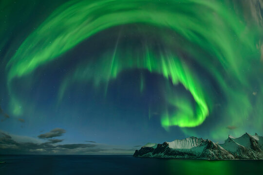Snowcapped mountains and sea under aurora borealis at night in Senja island, Troms, Norway