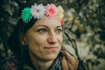 A woman with blue eyes and a colorful flower crown gazes thoughtfully. She stands outdoors,...