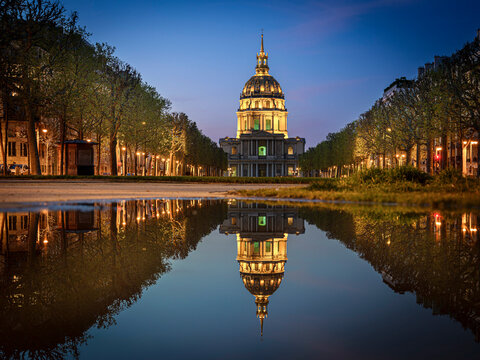 France, Ile-de-France, Paris, Dome des Invalides reflecting in puddle of water at dusk