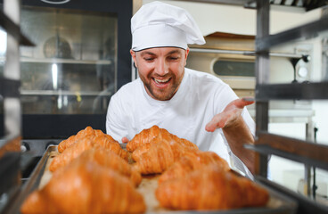 Smiling baker holding tray with fresh cooked croissants in bakehouse