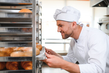 Male baker holding a tray of baked breads in bakery shop