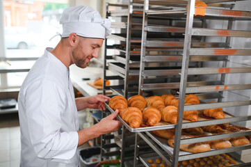 Smiling baker holding tray with fresh cooked croissants in bakehouse