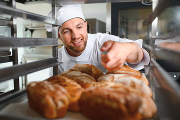 Male baker holding a tray of baked breads in bakery shop