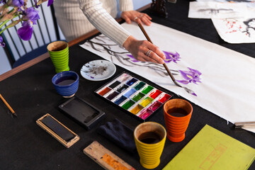 Hand of woman artist painting iris flowers on white paper at home