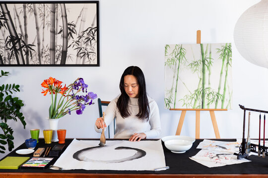 Focused artist painting sumi circle on white paper at home