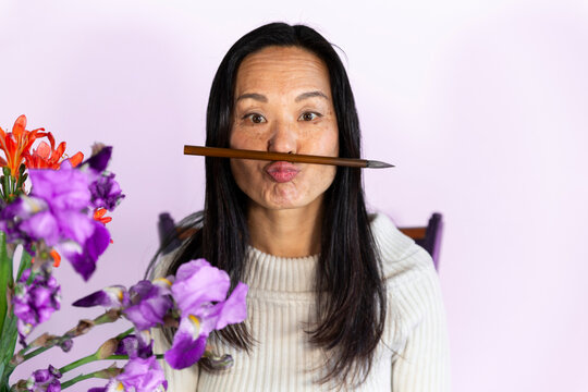 Playful woman balancing paintbrush and puckering lips sitting on chair at home
