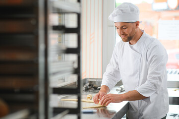 A male baker makes croissants in the bakery kitchen