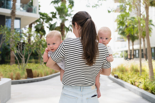 Mother with ponytail carrying twin sons in back yard