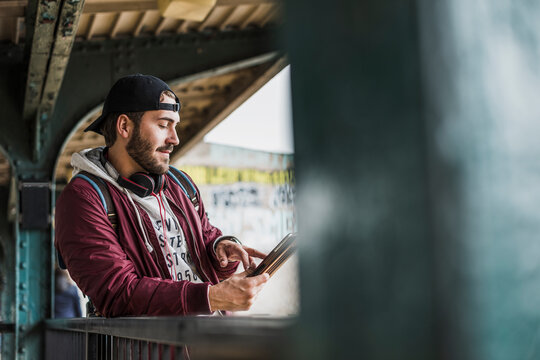 Young man using digital tablet leaning on railing at station