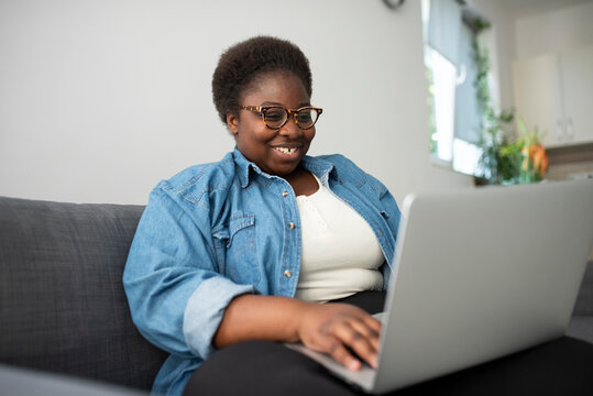 Smiling plus sized woman working on laptop in living room at home