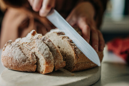 Hands of woman cutting fresh bread in kitchen