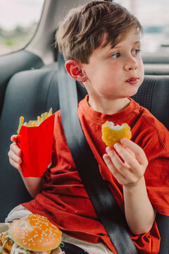 Cute boy holding french fries and eating burger in car