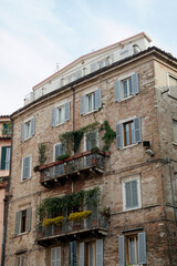Beautiful old brick building facade with balconies, greenery and shutters on the windows in Perugia (Italy).