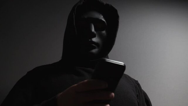 Phone Scammers, man in a mask with a phone, anonymous hacker performing phishing, identity theft via mobile phone, danger to privacy and security