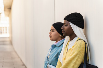 Portrait of two serious and thoughtful muslim women leaning against a building wall