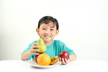 Fototapeta premium A cheerful boy in green shirt smiles while holding fresh fruits,including a pear,apple,orange,and banana.Ideal for promoting healthy eating,fruit benefits,nutrition education,and children's wellness
