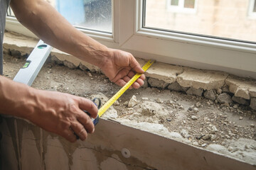 Worker measuring old window sill before renovation at home.