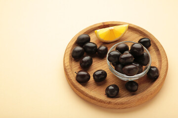 Black olives with lemon on wooden plate on beige background