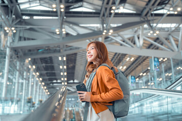 Asian tourist woman traveller with backpack holding mobile phone while stand on moving walkway in airport terminal, Tourist journey trip concept.