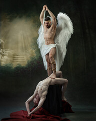 Man with angel wings stands over another man, holding sword aloft as light beams shine through...