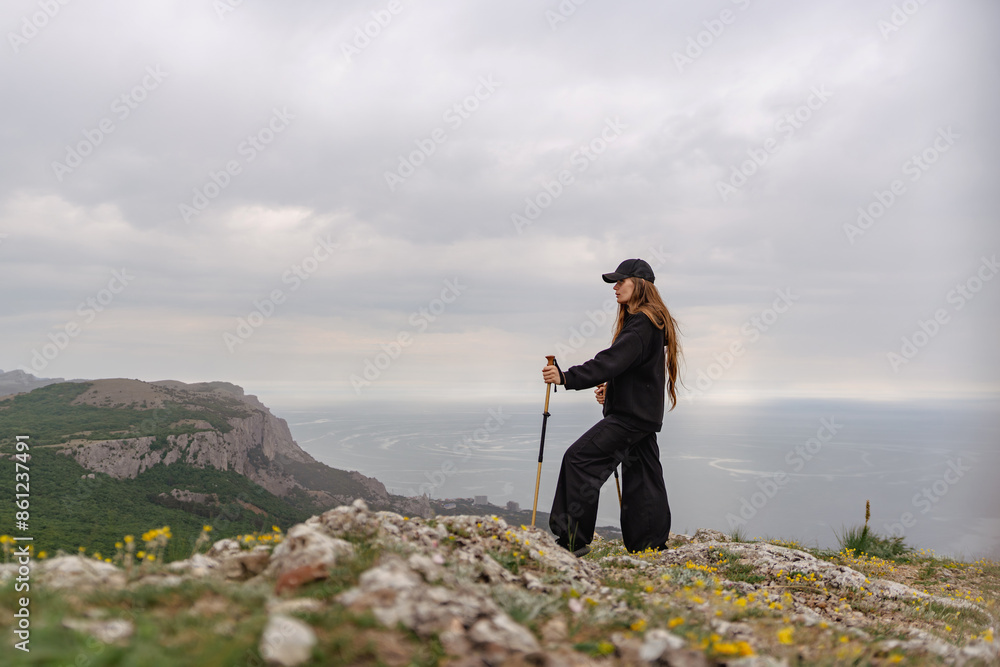 Wall mural A woman is standing on a rocky hill overlooking the ocean