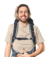 Young Caucasian hiker with backpack touches tummy, smiles gently, eating and satisfaction concept.