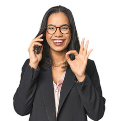 Latina in suit with phone in studio cheerful and confident showing ok gesture.