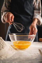 Close-up of female hands beating eggs in a transparent bowl using a whisk. Dark background.