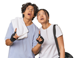 Young interracial athletic couple in studio pointing upside with opened mouth.