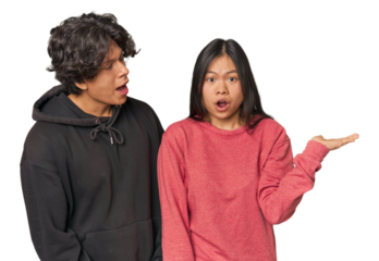 Young interracial couple in studio impressed holding copy space on palm.