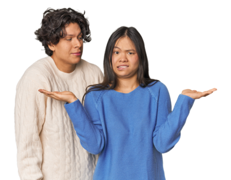 Young interracial couple in studio confused and doubtful shrugging shoulders to hold a copy space.
